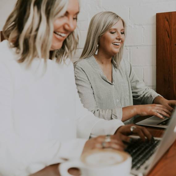 two blonde haired women laughing and typing on laptops