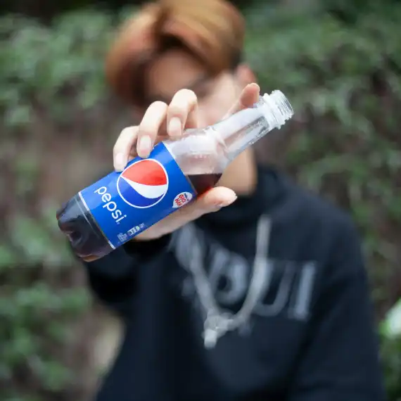 boy holding a bottle of pepsi towards the camera