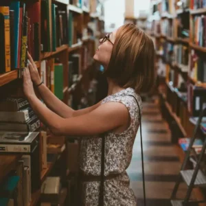 a woman looking at books standing between bookshelves