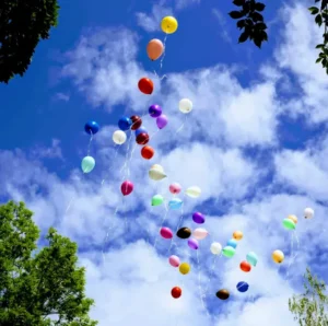 balloons floating in a blue sky surrounded by clouds and trees