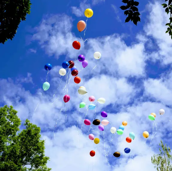 balloons floating in a blue sky surrounded by clouds and trees