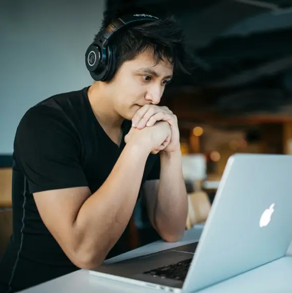 man wearing headphones sits at desk looking at laptop screen