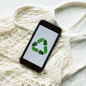 smartphone-with-recycling-sign-on-screen-placed-on-white-mesh-bag-on-marble-table